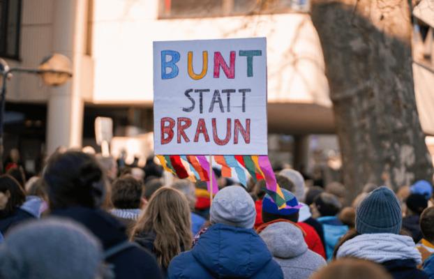 Eine Menschenmenge hält ein buntes Schild mit der Aufschrift 'BUNT STATT BRAUN' während einer Demonstration. (c)Sabah_Bahira